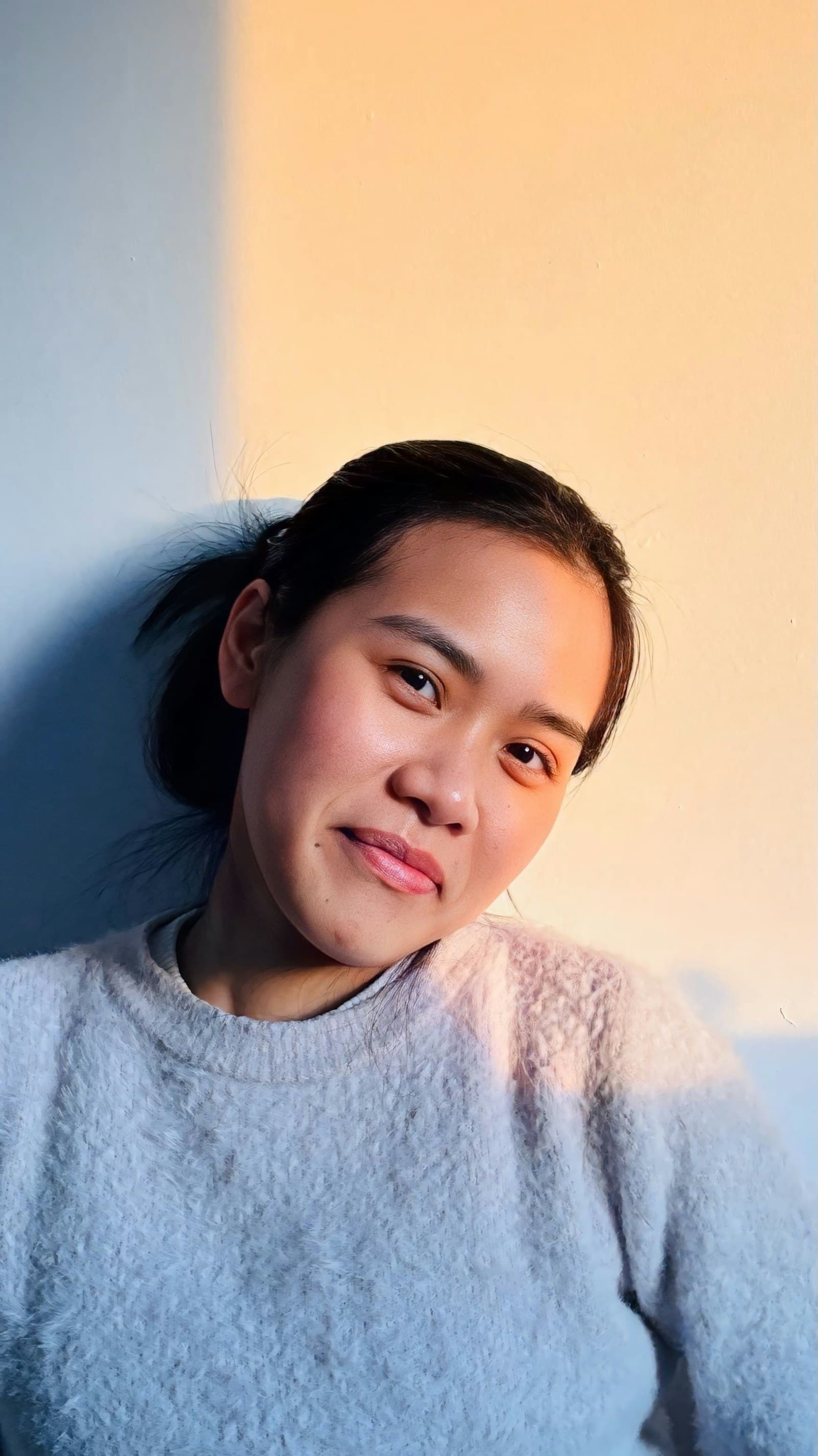 A woman smiling in soft warm window light. Photo by Tan Duong on Unsplash.