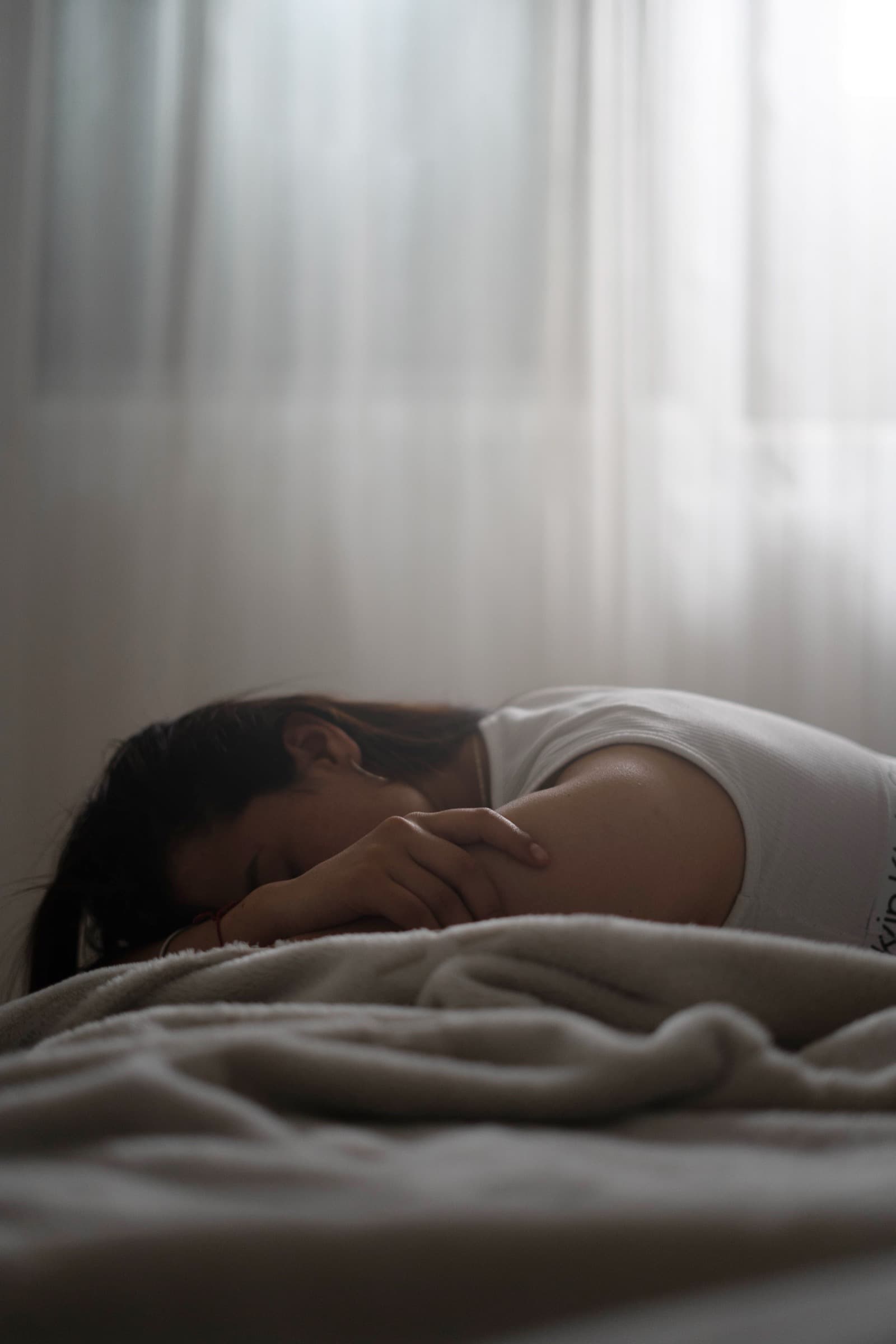 A woman sleeping under a soft blanket in a sunlit bedroom. Photo by Alan Cordero on Pexels.