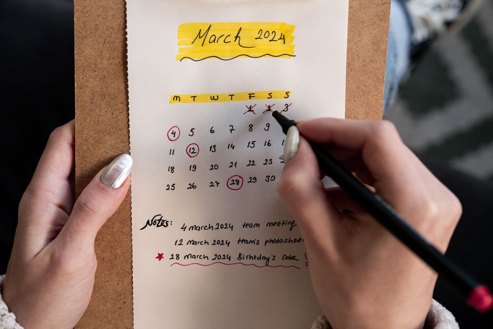Hands crossing off days on a handwritten monthly calendar. Photo by Ahmed on Pexels.