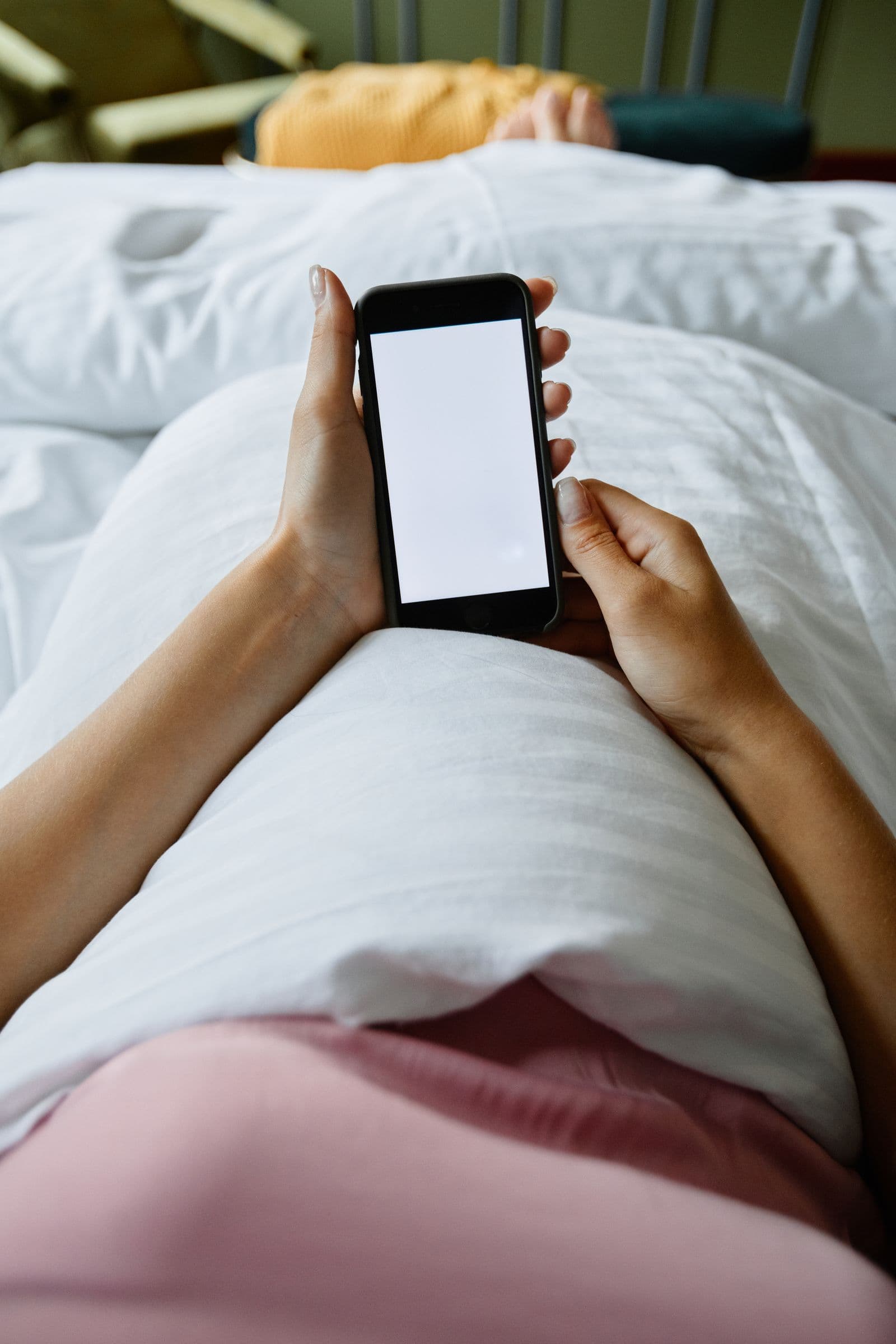 A woman lying in bed using a smartphone at night. Photo by Marcus Aurelius on Pexels.