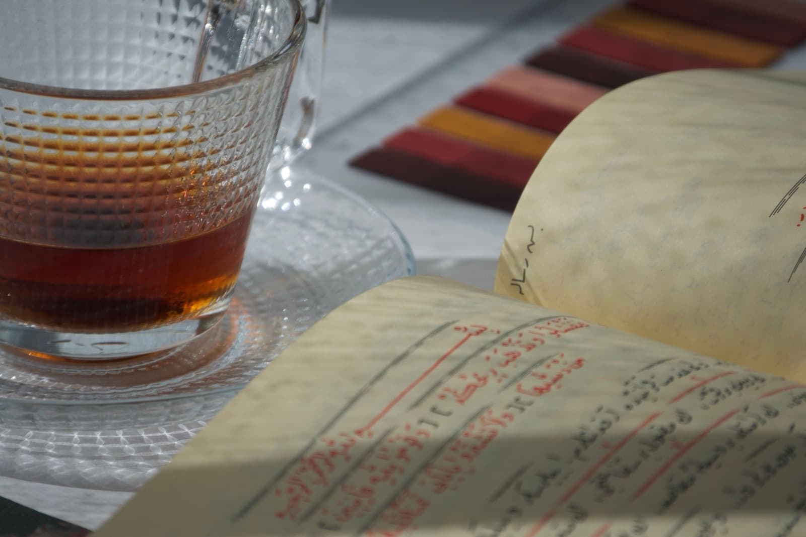 An open journal beside a glass cup of tea in warm afternoon sunlight. Photo by Muhtelifane on Pexels.
