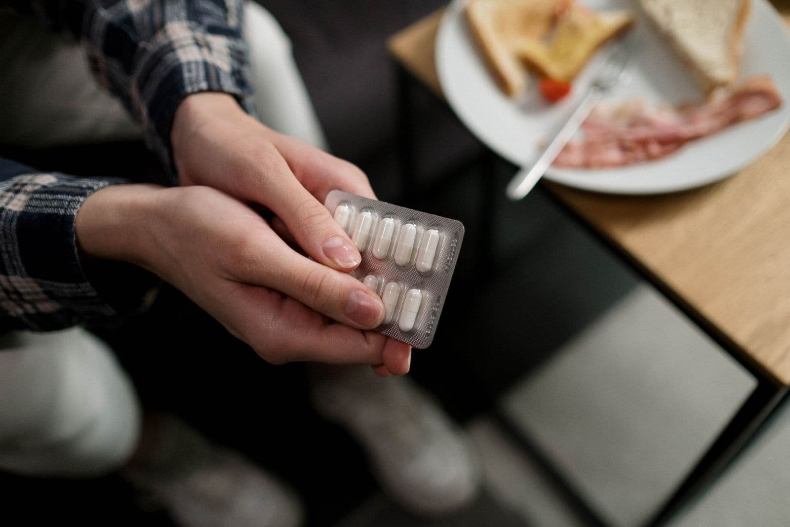 A person holding a blister pack of capsules at a breakfast table. Photo by Ron Lach on Pexels.