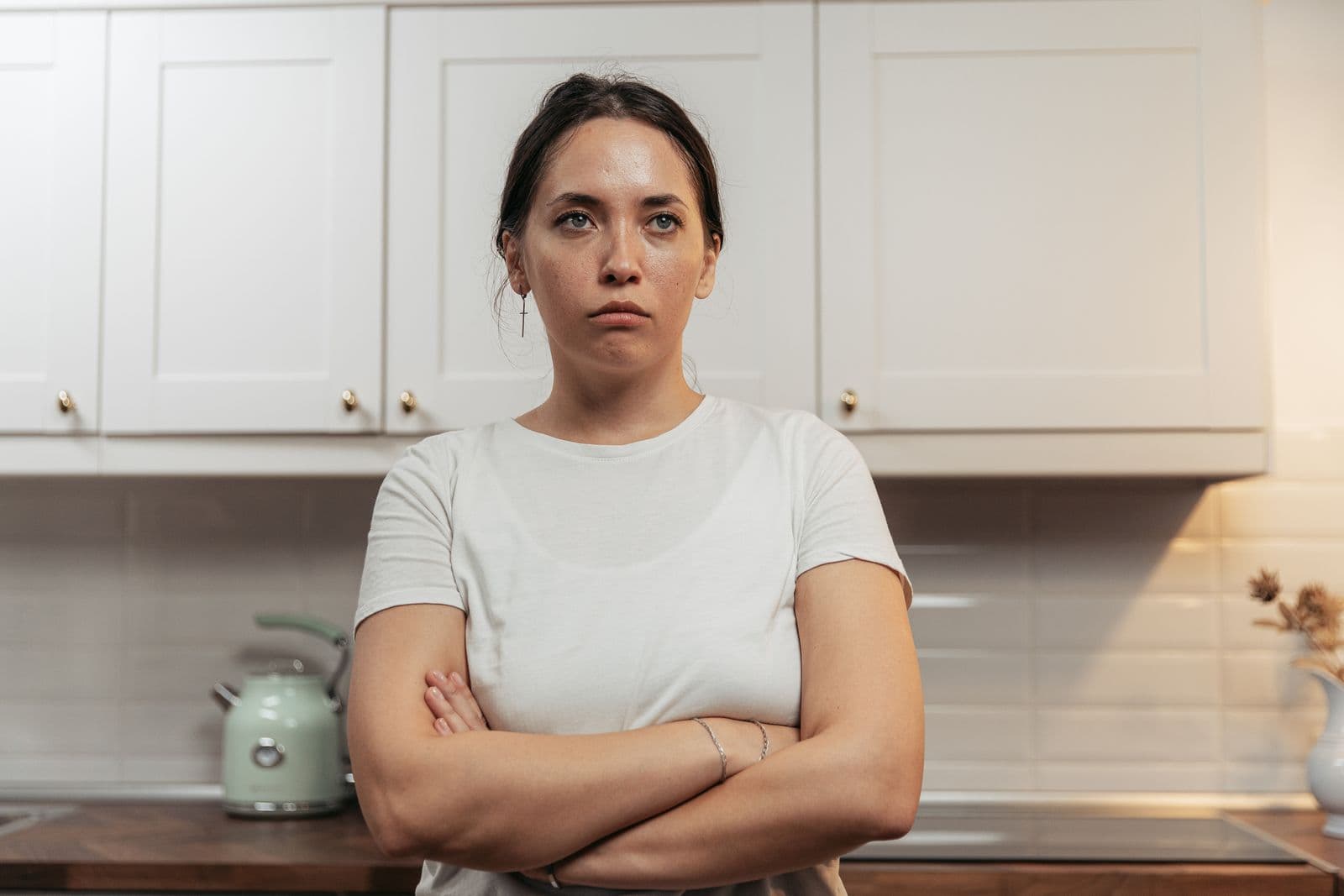 A woman standing in a kitchen with her arms crossed and a tense expression. Photo by SHVETS production on Pexels.