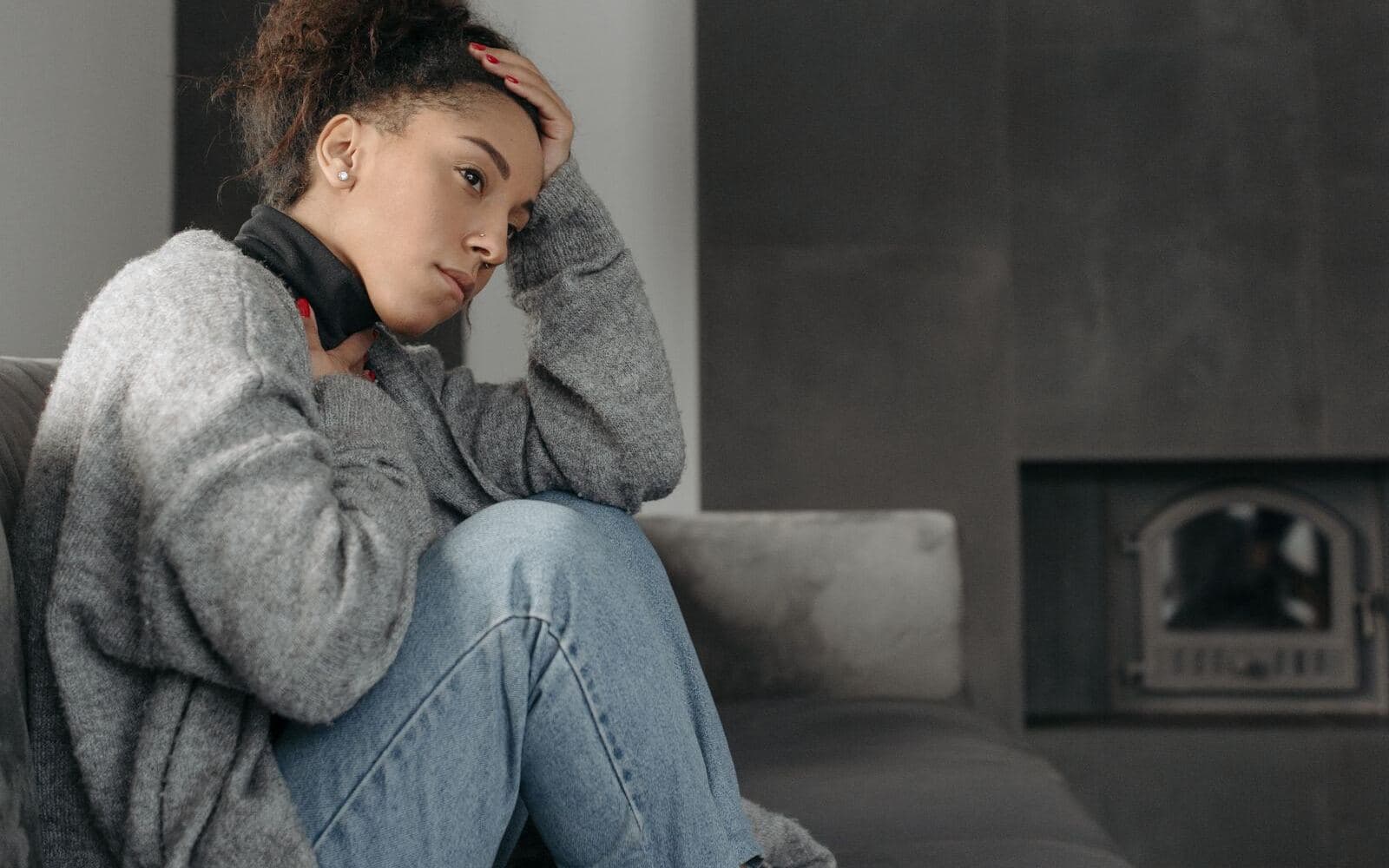 A woman in a grey cardigan sitting on a sofa with one hand resting against her head. Photo by Pavel Danilyuk on Pexels.