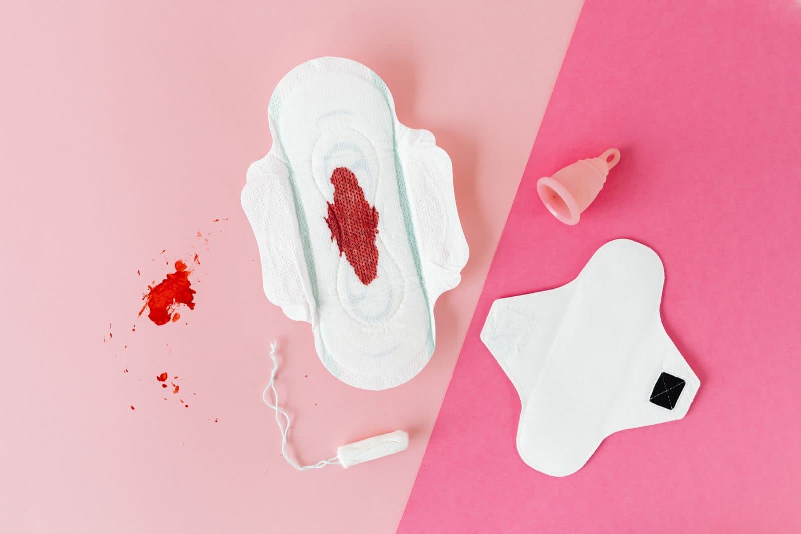 Flat lay of a menstrual pad, a menstrual cup and a tampon on a pink background. Photo by Karolina Grabowska on Pexels.