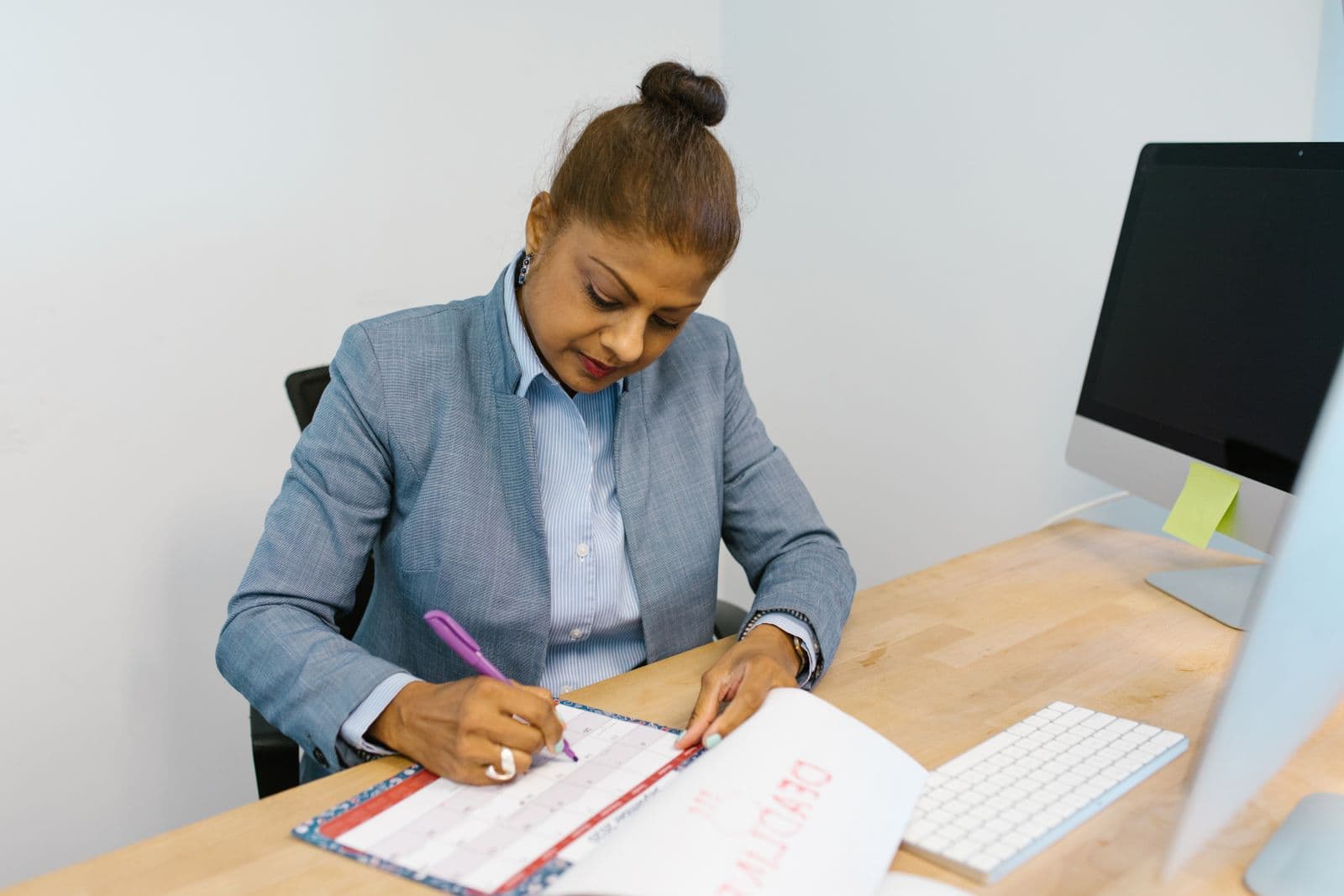 A woman marking dates in a paper calendar at a desk. Photo by RDNE Stock project on Pexels.