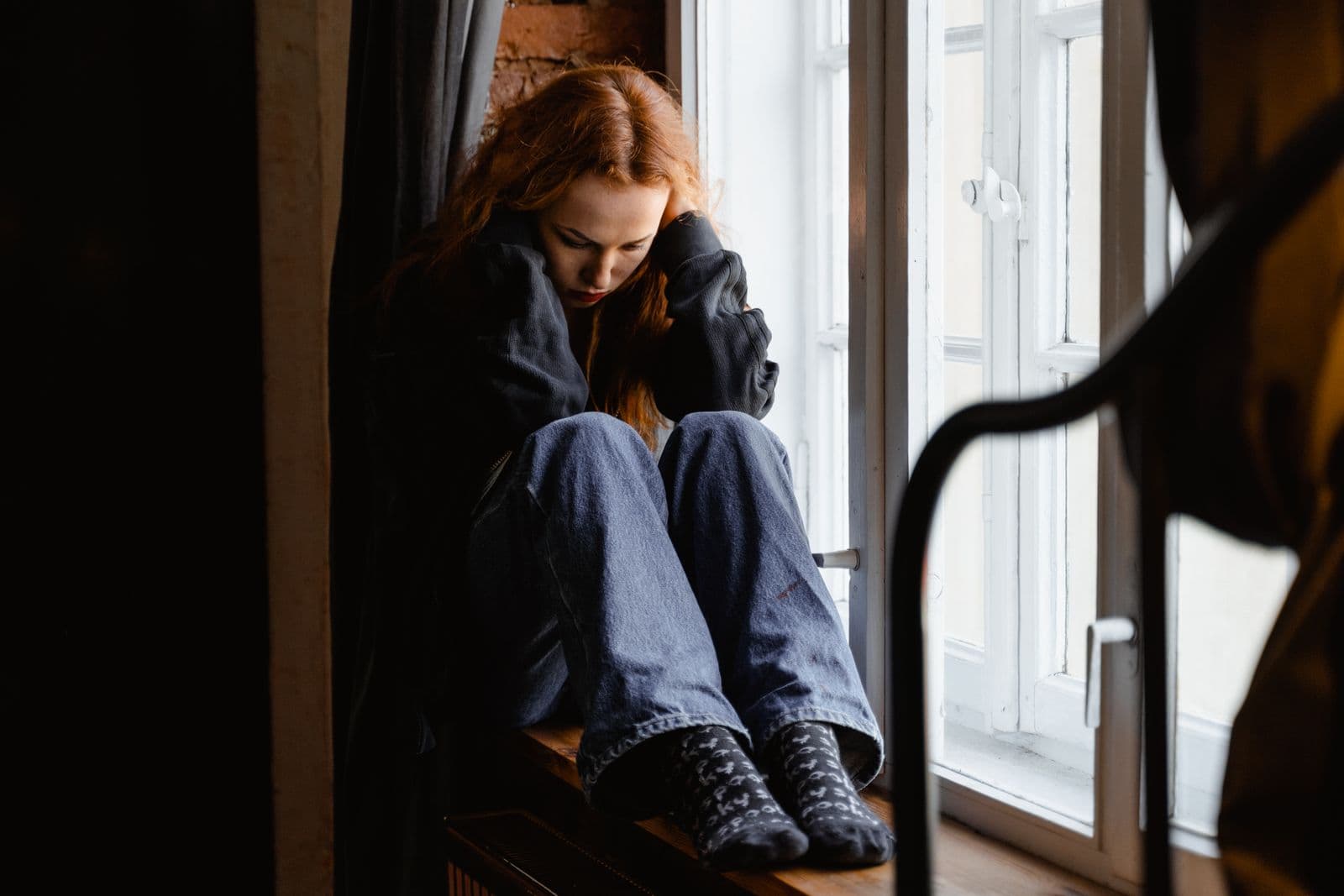 A woman sitting pensively by a window. Photo by MART PRODUCTION on Pexels.