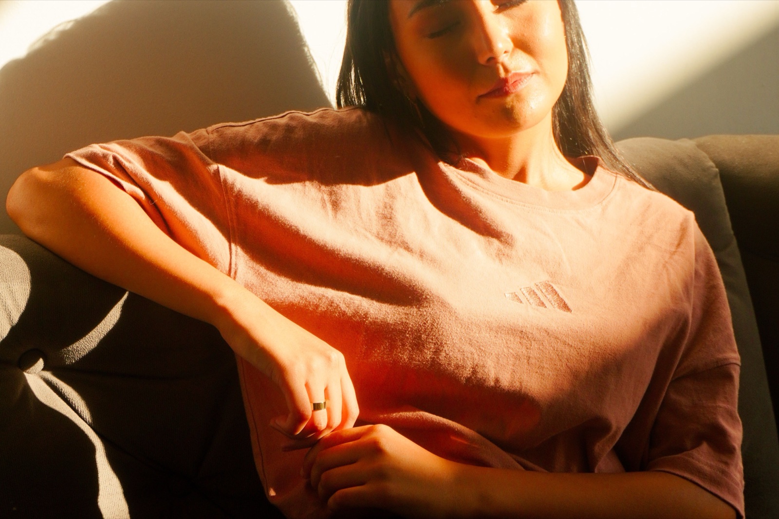 A woman in a muted pink top resting on a sofa in warm sunlight