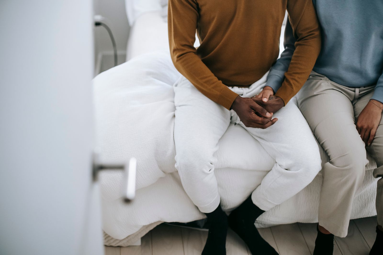 A couple sitting on a bed at home, holding hands