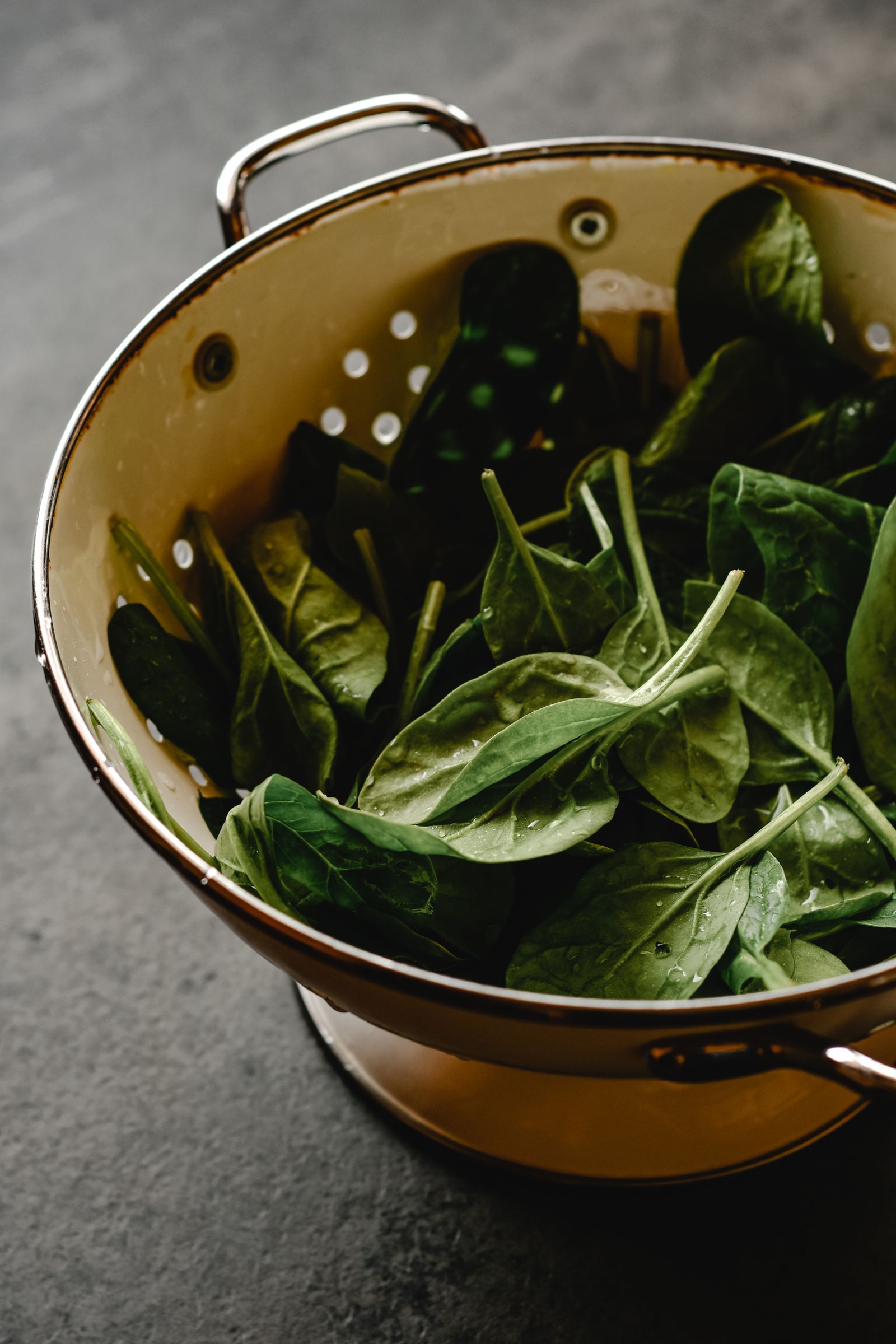 Freshly washed spinach leaves in a colander in a kitchen