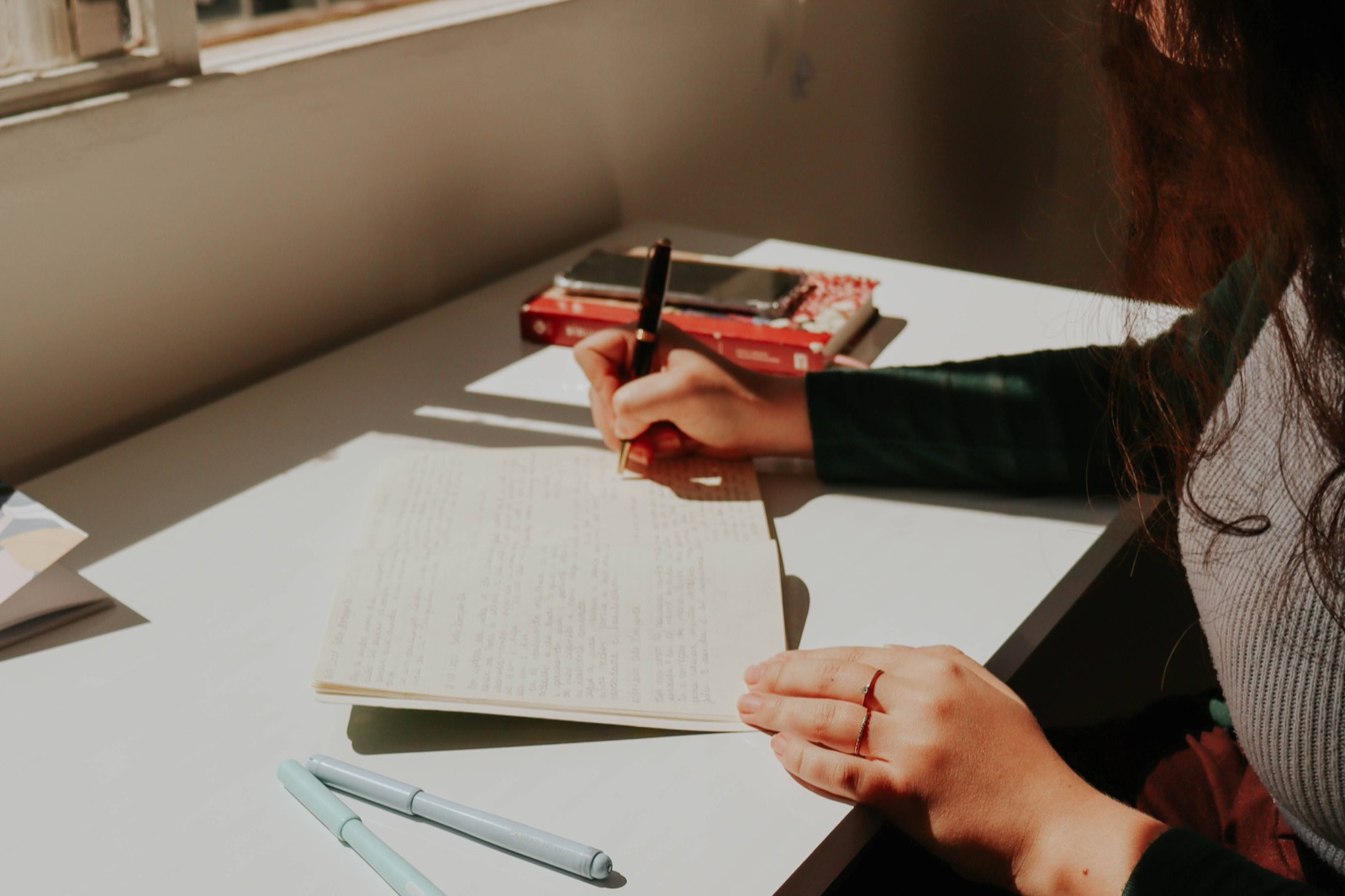 A woman writing in a notebook beside a sunlit window