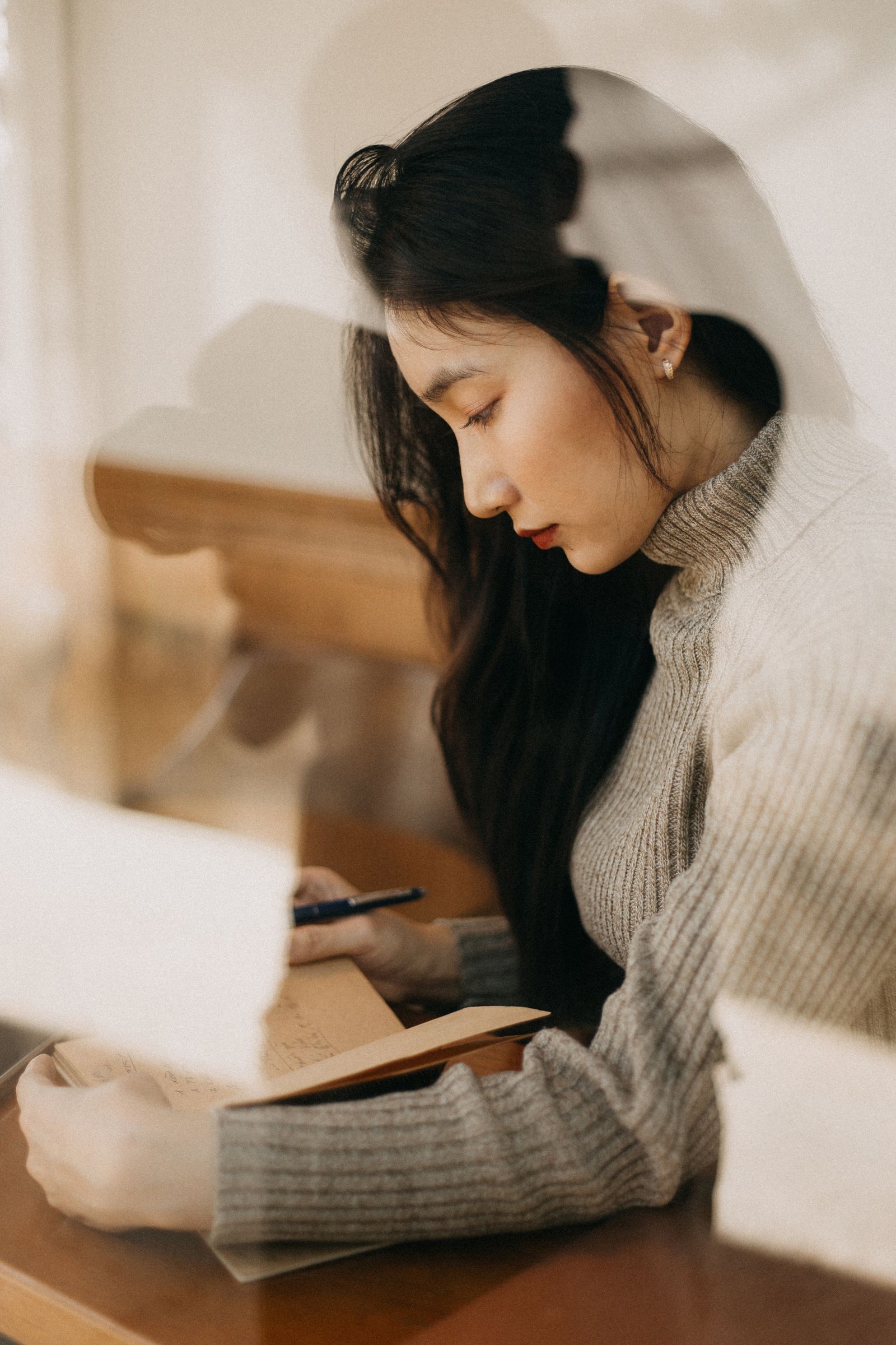 A woman in a soft sweater writing in a journal beside a sunlit window