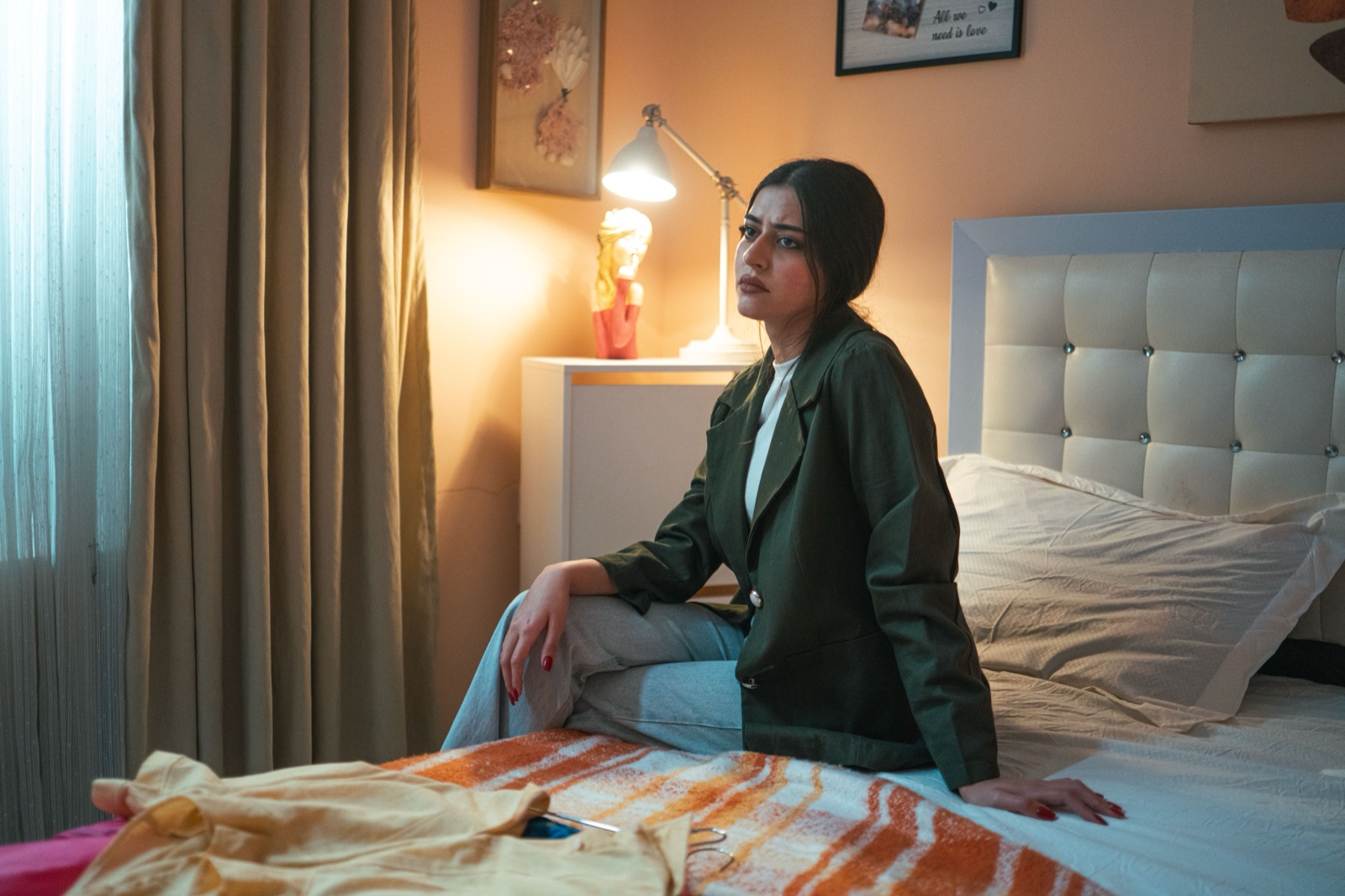 A thoughtful woman in a green jacket sitting on a bed in warm light