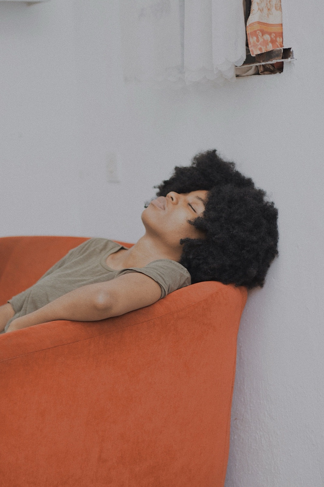 A woman resting peacefully on an orange sofa in soft natural light