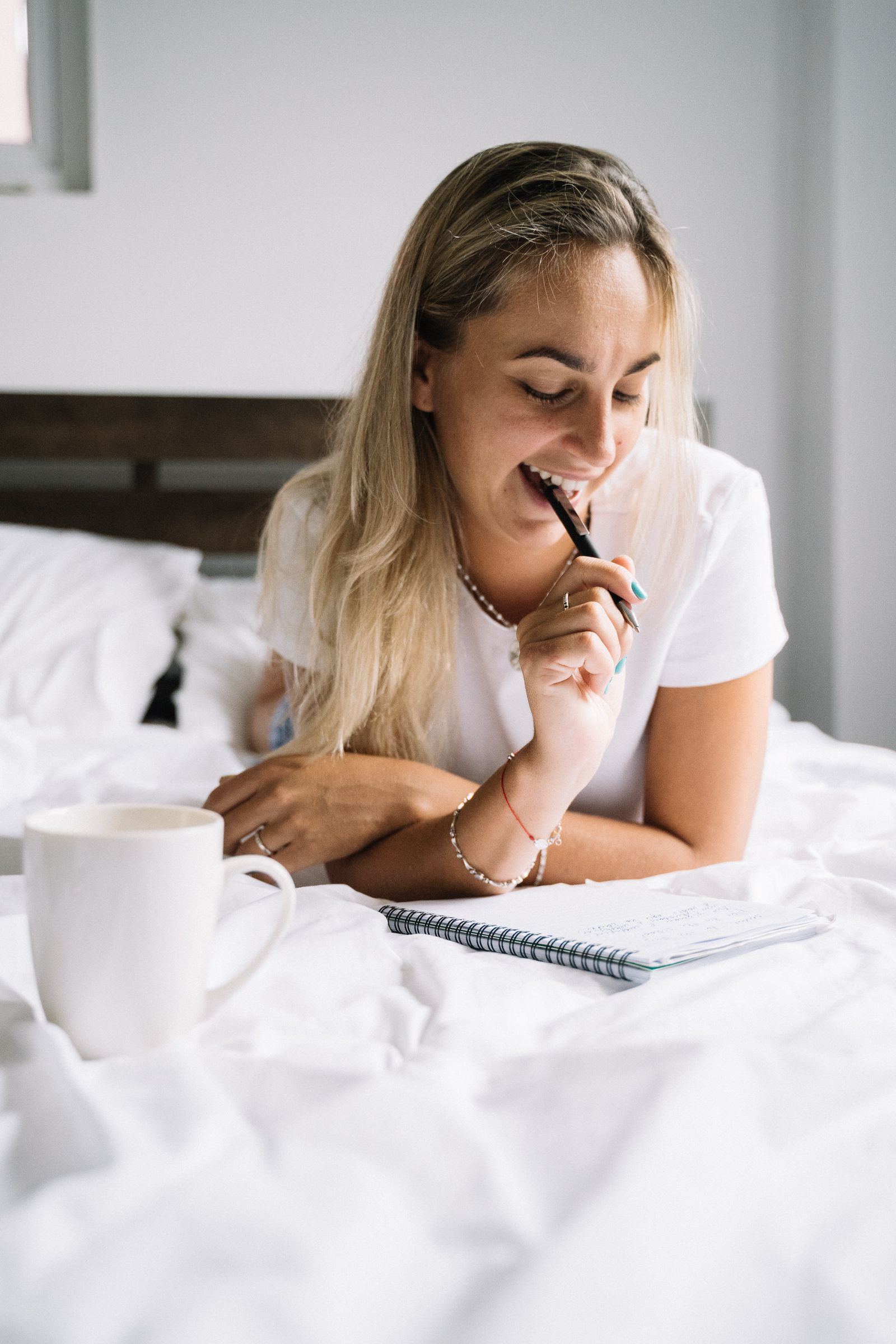 A woman writing in a journal on a bed beside a warm drink